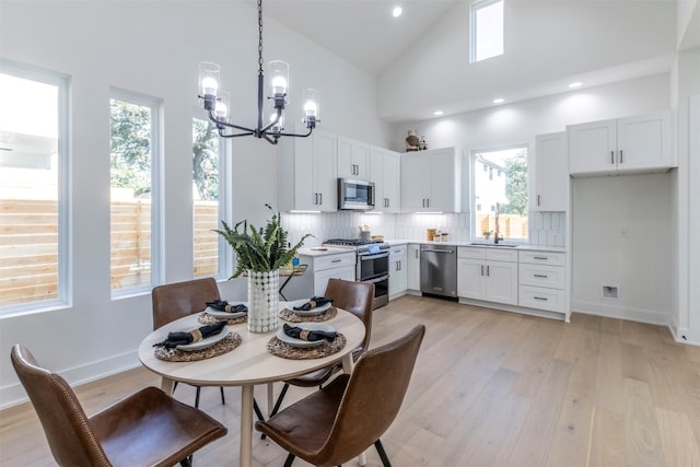 dining space with sink, light wood-type flooring, high vaulted ceiling, and a notable chandelier