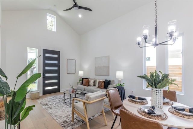 living room with high vaulted ceiling, ceiling fan with notable chandelier, and light hardwood / wood-style floors