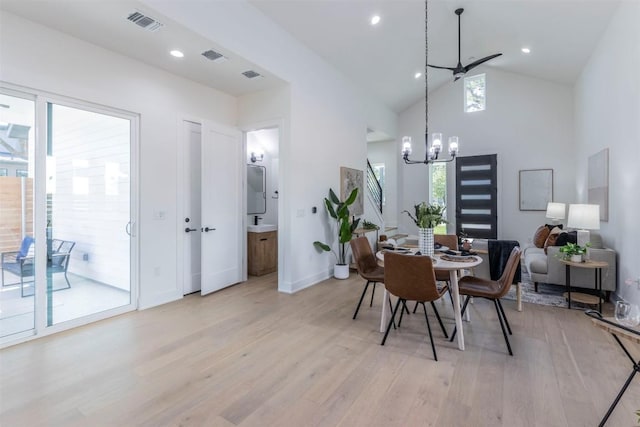 dining space with high vaulted ceiling, light wood-style flooring, visible vents, and ceiling fan with notable chandelier