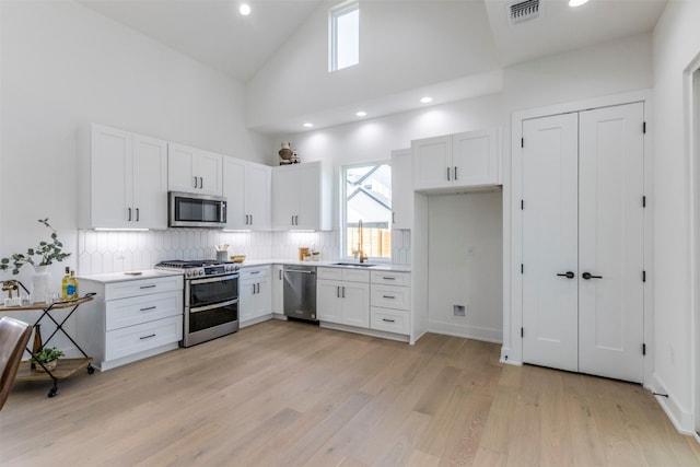 kitchen with backsplash, high vaulted ceiling, appliances with stainless steel finishes, light hardwood / wood-style flooring, and white cabinets