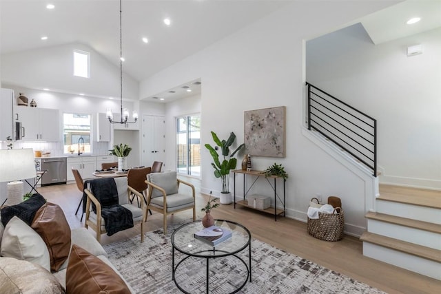 living room featuring baseboards, stairway, an inviting chandelier, light wood-style floors, and high vaulted ceiling