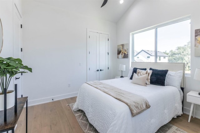 bedroom featuring light wood-style floors, a closet, high vaulted ceiling, and baseboards