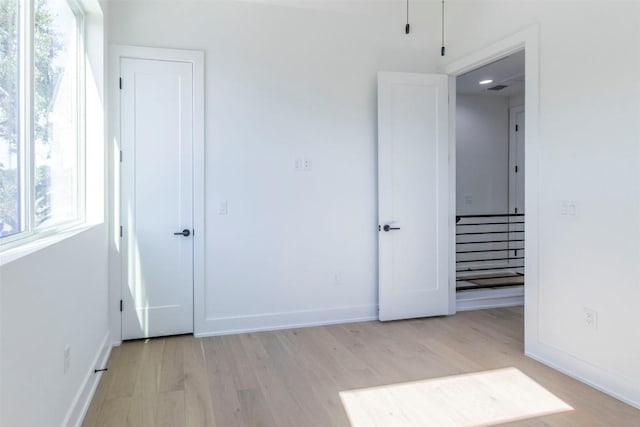 unfurnished bedroom featuring light wood-style floors, multiple windows, and baseboards