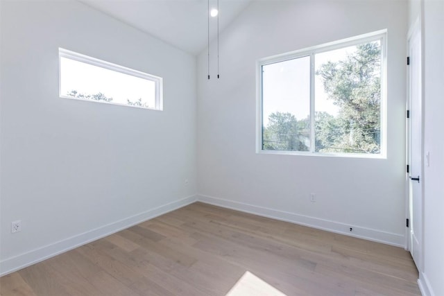 empty room with light wood-type flooring, a healthy amount of sunlight, vaulted ceiling, and baseboards