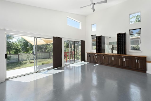 unfurnished living room featuring a towering ceiling, finished concrete flooring, and a ceiling fan