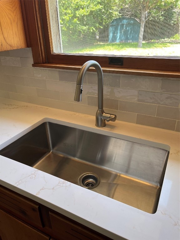 interior details featuring backsplash, light stone counters, and sink