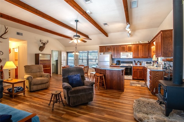 kitchen featuring a wood stove, white appliances, a kitchen island, a breakfast bar, and hardwood / wood-style floors