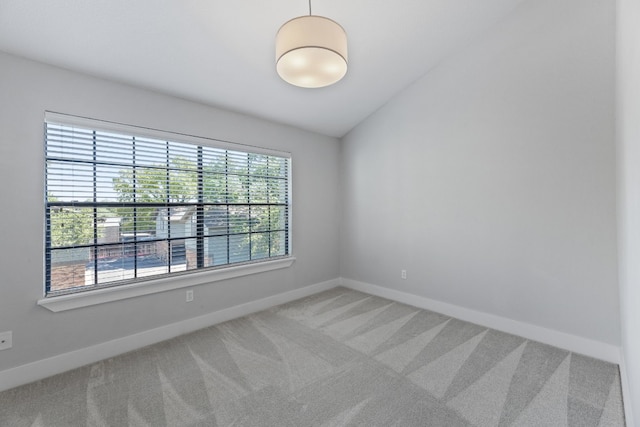 empty room featuring vaulted ceiling, carpet, and baseboards