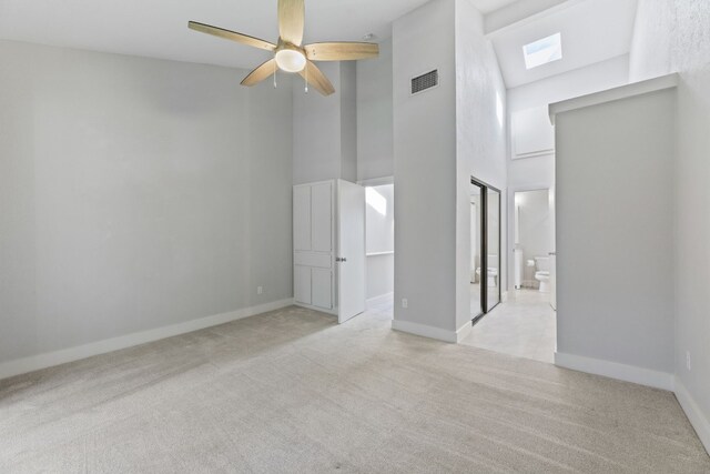 carpeted spare room with a skylight, ceiling fan, and a towering ceiling