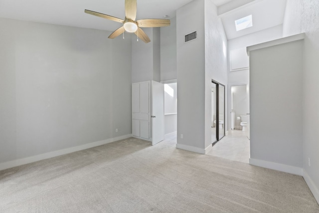 interior space with light carpet, baseboards, visible vents, a towering ceiling, and ensuite bath