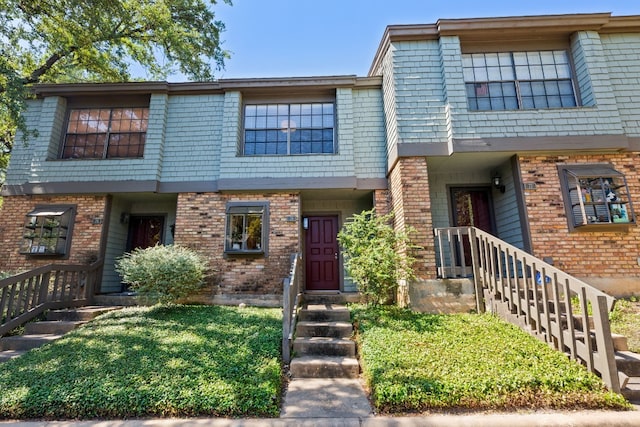 townhome / multi-family property with a front yard, mansard roof, and brick siding