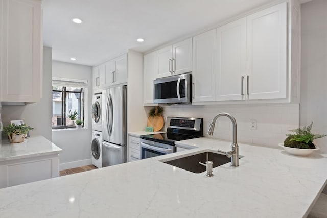 kitchen with light stone counters, stacked washer / dryer, white cabinetry, and stainless steel appliances