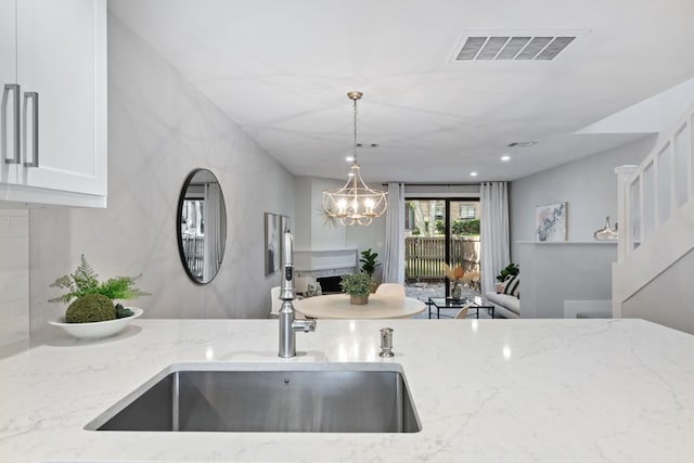 kitchen with a notable chandelier, light stone counters, sink, hanging light fixtures, and white cabinetry