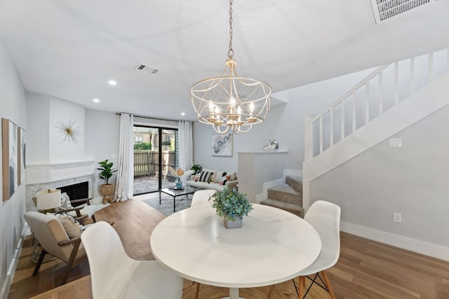 dining room with wood-type flooring, a notable chandelier, and a fireplace