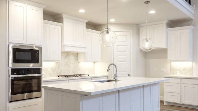 kitchen featuring a kitchen island with sink, white cabinets, sink, hanging light fixtures, and stainless steel appliances