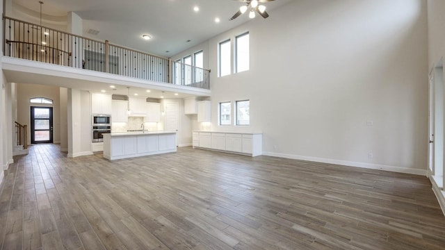 unfurnished living room featuring a high ceiling, sink, ceiling fan, and wood-type flooring