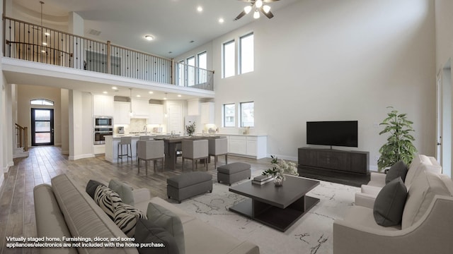 living room with a towering ceiling, light hardwood / wood-style flooring, and ceiling fan