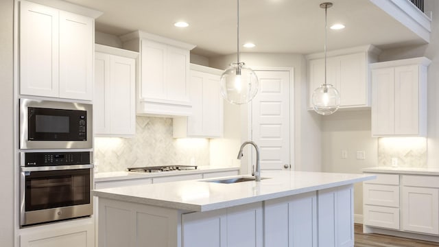 kitchen featuring pendant lighting, sink, white cabinets, a kitchen island with sink, and stainless steel appliances