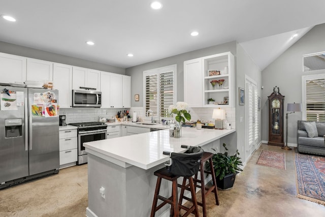 kitchen with appliances with stainless steel finishes, a kitchen bar, tasteful backsplash, white cabinets, and kitchen peninsula