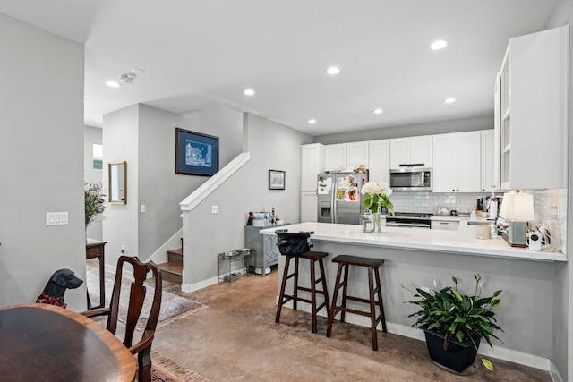 kitchen featuring a kitchen breakfast bar, tasteful backsplash, white cabinets, appliances with stainless steel finishes, and kitchen peninsula