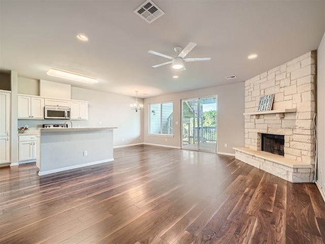 unfurnished living room featuring ceiling fan with notable chandelier, dark hardwood / wood-style floors, and a stone fireplace