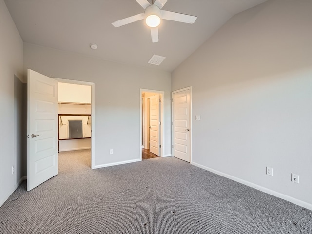 unfurnished bedroom with a walk in closet, ceiling fan, carpet floors, and vaulted ceiling