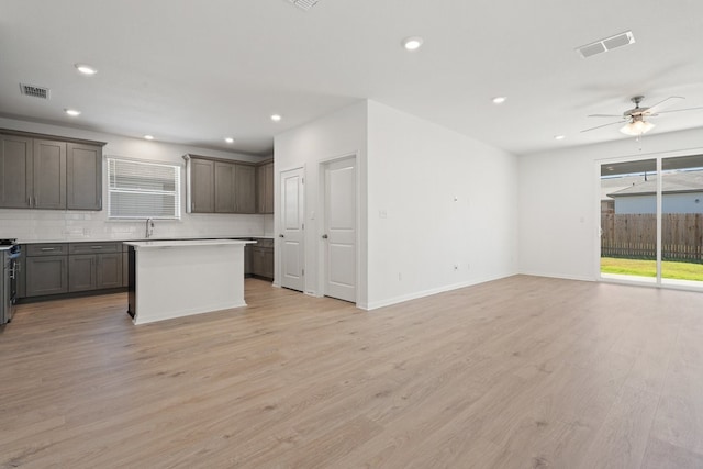 kitchen with a kitchen island, backsplash, stainless steel stove, light wood-type flooring, and ceiling fan