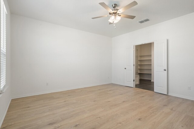 unfurnished bedroom with a closet, ceiling fan, light hardwood / wood-style flooring, and a walk in closet