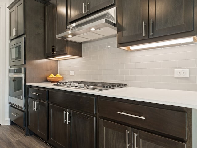 kitchen featuring dark brown cabinetry, stainless steel appliances, dark wood-type flooring, and tasteful backsplash