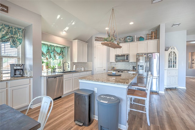 kitchen with vaulted ceiling, light hardwood / wood-style flooring, a center island, stainless steel appliances, and white cabinetry