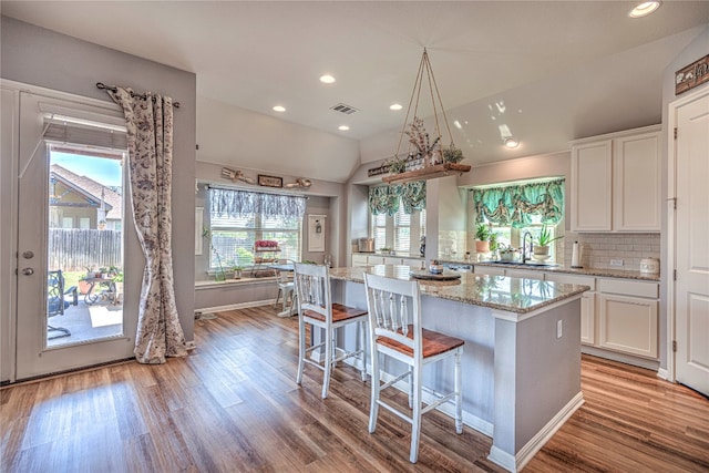 kitchen featuring white cabinets, light stone countertops, light hardwood / wood-style floors, lofted ceiling, and a kitchen island