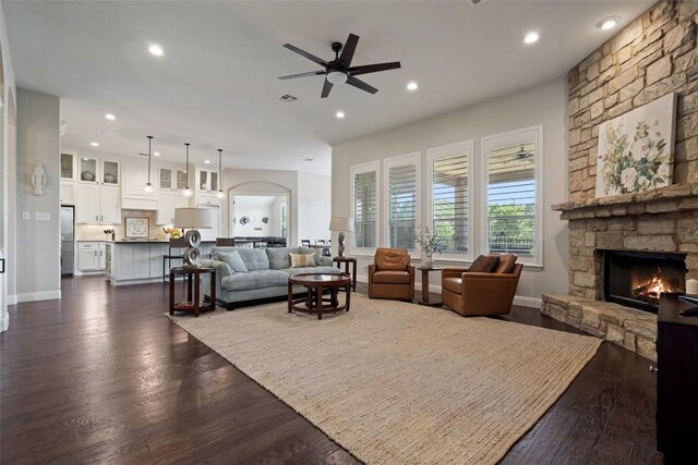 living room with ceiling fan, a stone fireplace, and dark hardwood / wood-style flooring