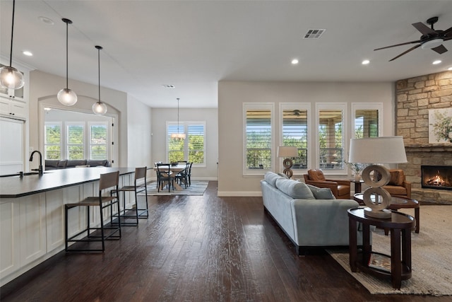 living room with ceiling fan, dark wood-type flooring, a stone fireplace, and sink