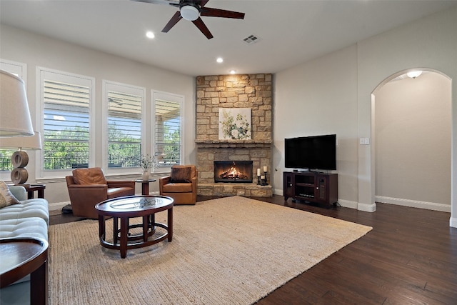 living room featuring ceiling fan, a fireplace, and dark wood-type flooring