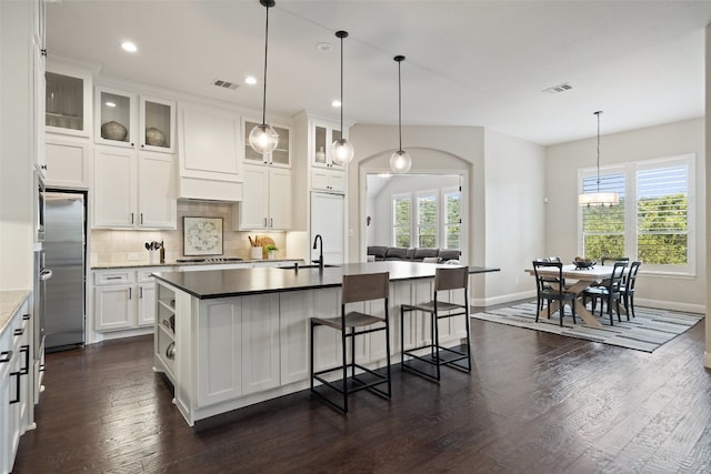 kitchen with backsplash, dark wood-type flooring, a center island with sink, and sink