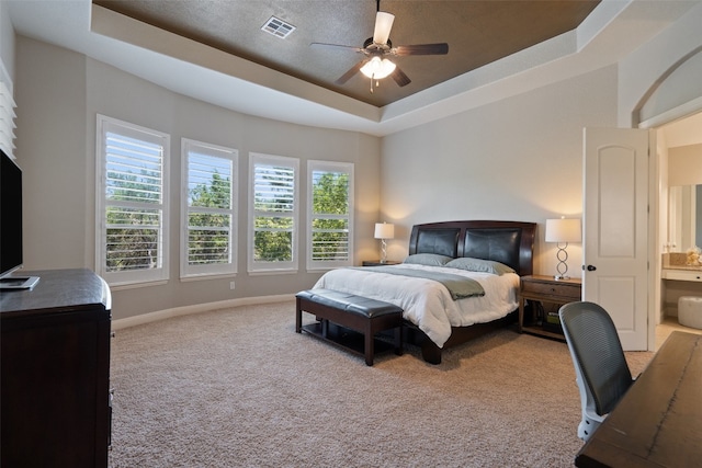 carpeted bedroom with ceiling fan, a raised ceiling, and ensuite bath