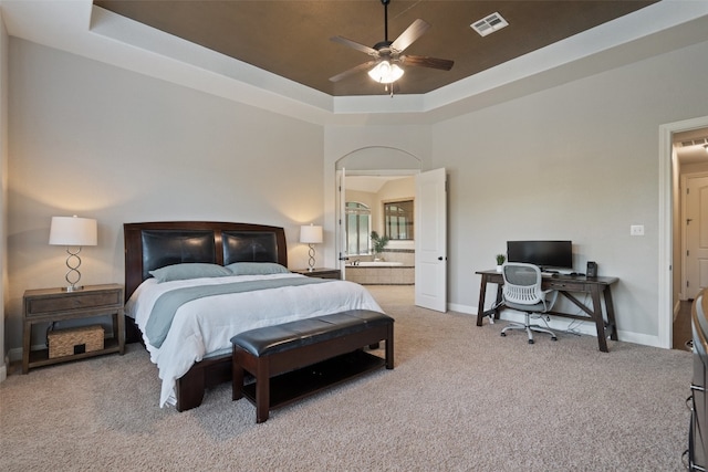 carpeted bedroom with ceiling fan, connected bathroom, a high ceiling, and a tray ceiling