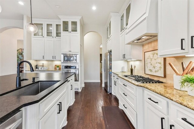 1104 Lions Lair, Leander, TX 78641 - kitchen featuring arched walkways, appliances with stainless steel finishes, custom range hood, white cabinets, and dark stone counters