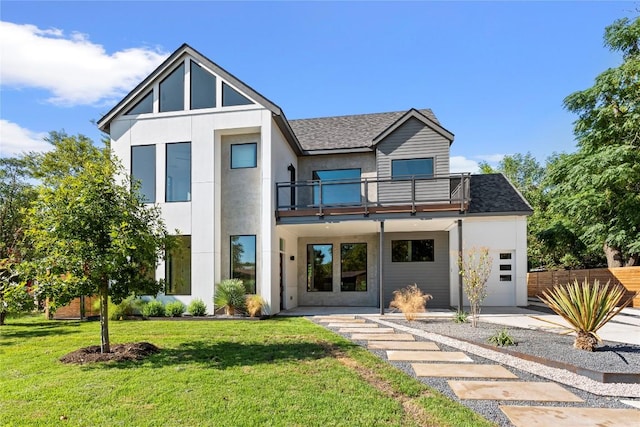 rear view of property featuring a shingled roof, a lawn, a balcony, and fence