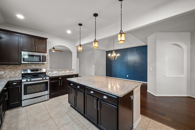 kitchen with stainless steel appliances, light tile patterned flooring, a center island, and light stone countertops