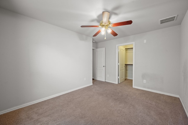 unfurnished bedroom with a walk in closet, carpet flooring, a closet, and ceiling fan