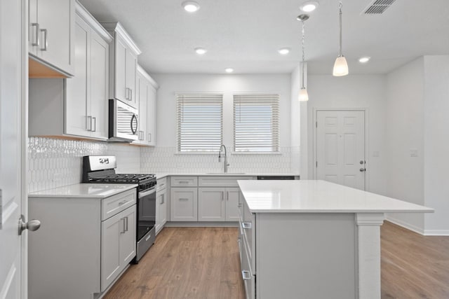 kitchen featuring a kitchen island, light wood-type flooring, sink, pendant lighting, and stainless steel appliances