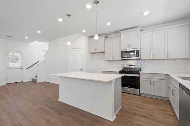 kitchen with appliances with stainless steel finishes, a center island, decorative light fixtures, white cabinets, and dark wood-type flooring