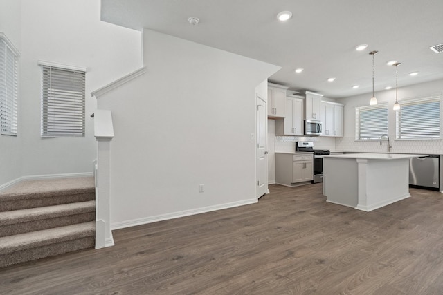 kitchen with dark hardwood / wood-style floors, appliances with stainless steel finishes, a kitchen island, and hanging light fixtures