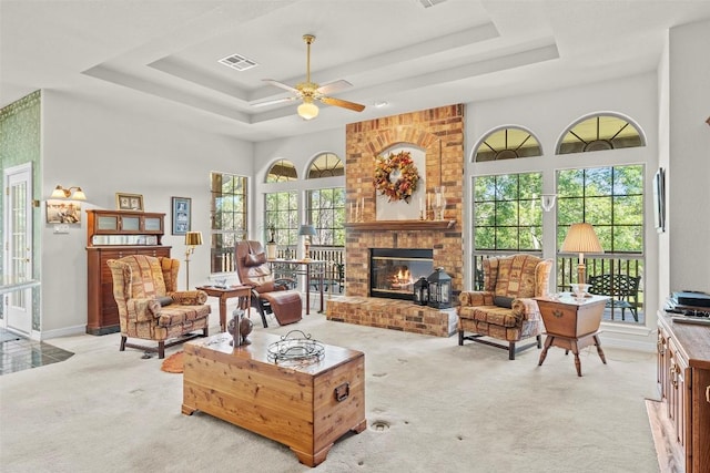 living area with light carpet, a tray ceiling, a brick fireplace, and visible vents