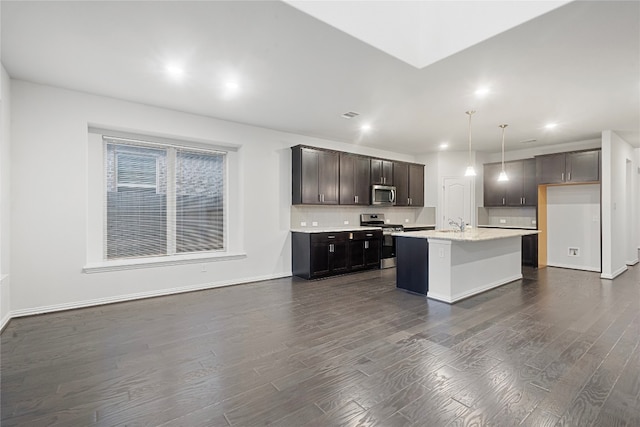 kitchen with stainless steel appliances, a kitchen island with sink, decorative light fixtures, and dark hardwood / wood-style floors