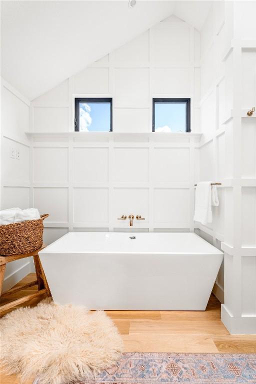 bathroom with a healthy amount of sunlight, vaulted ceiling, hardwood / wood-style flooring, and a tub