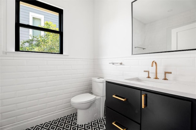 bathroom with wainscoting, vanity, toilet, and tile walls