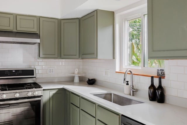 kitchen with decorative backsplash, green cabinets, stainless steel gas range oven, and sink