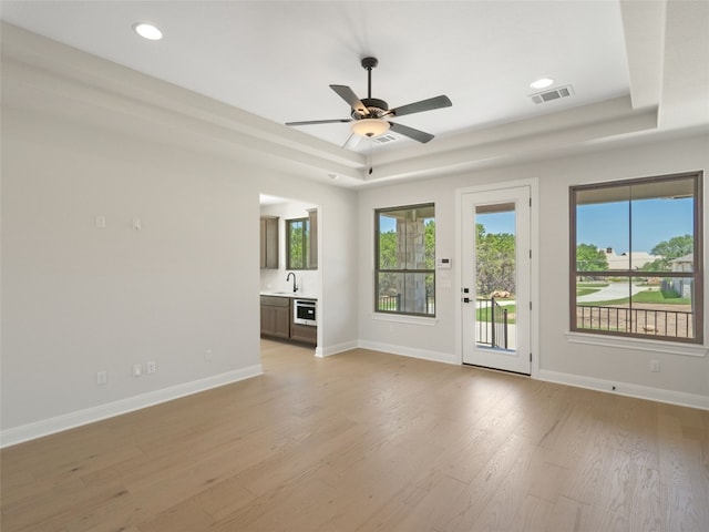 unfurnished room with ceiling fan, sink, light hardwood / wood-style flooring, and a tray ceiling